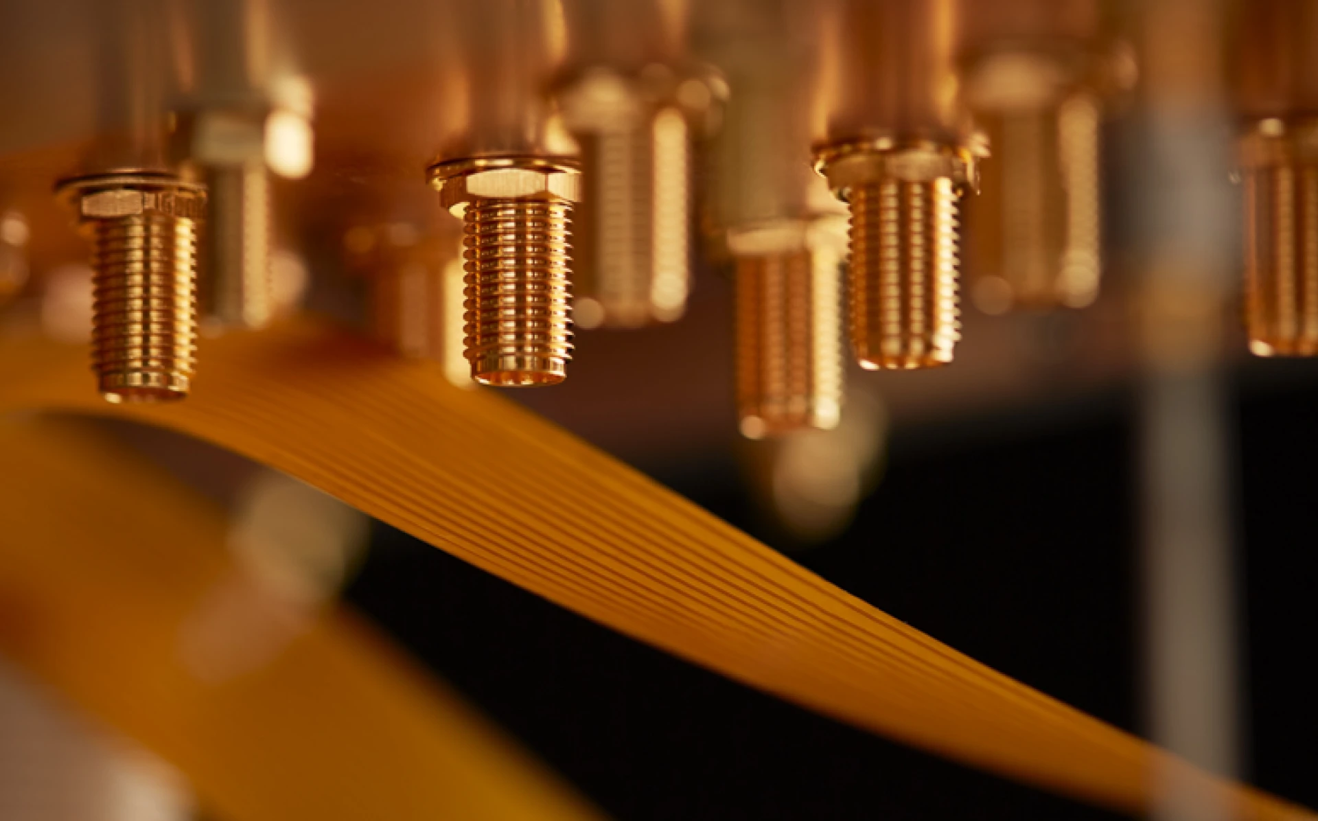 Gold-plated RF connectors and a flexible ribbon cable on a kiutra cryostat stage, lit warm against a dark background
