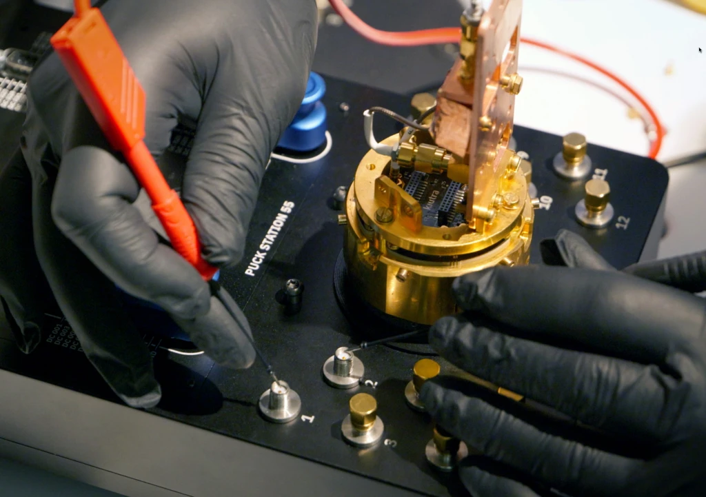Gloved hands testing DC pin connections on a Puck Station 55 panel with a multimeter probe.