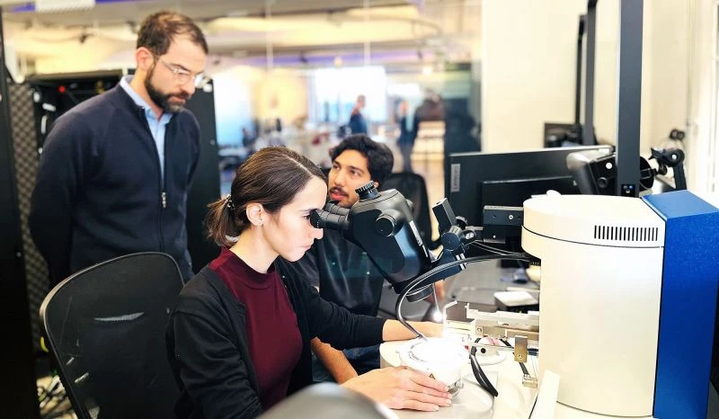 An engineer at the semi-automatic wire bonder in the kiutra characterization lab, two colleagues watching