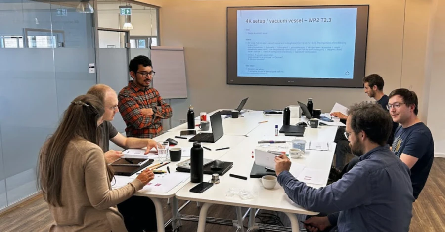 LEMON project workshop: eight team members around a meeting table, a slide on the 4K setup and vacuum vessel of work package 2 on the screen behind them