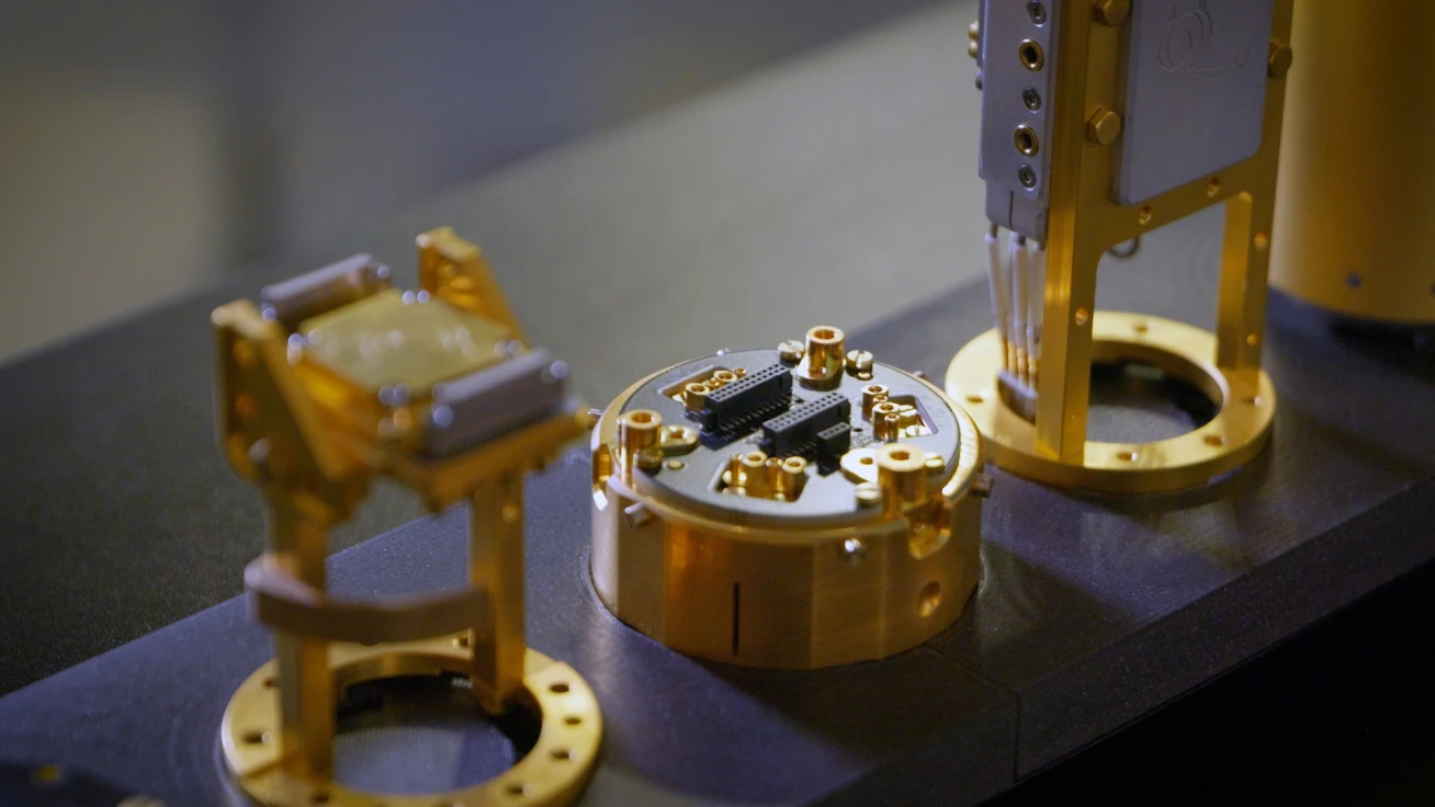 Gold-plated kiutra sample holders and a Puck 55 with a wire-bonded chip, side by side on a dark bench
