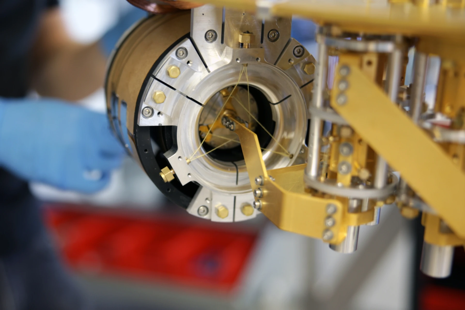 Close-up of a gold-plated ADR cooling stage with fine wiring, a gloved hand visible in the background